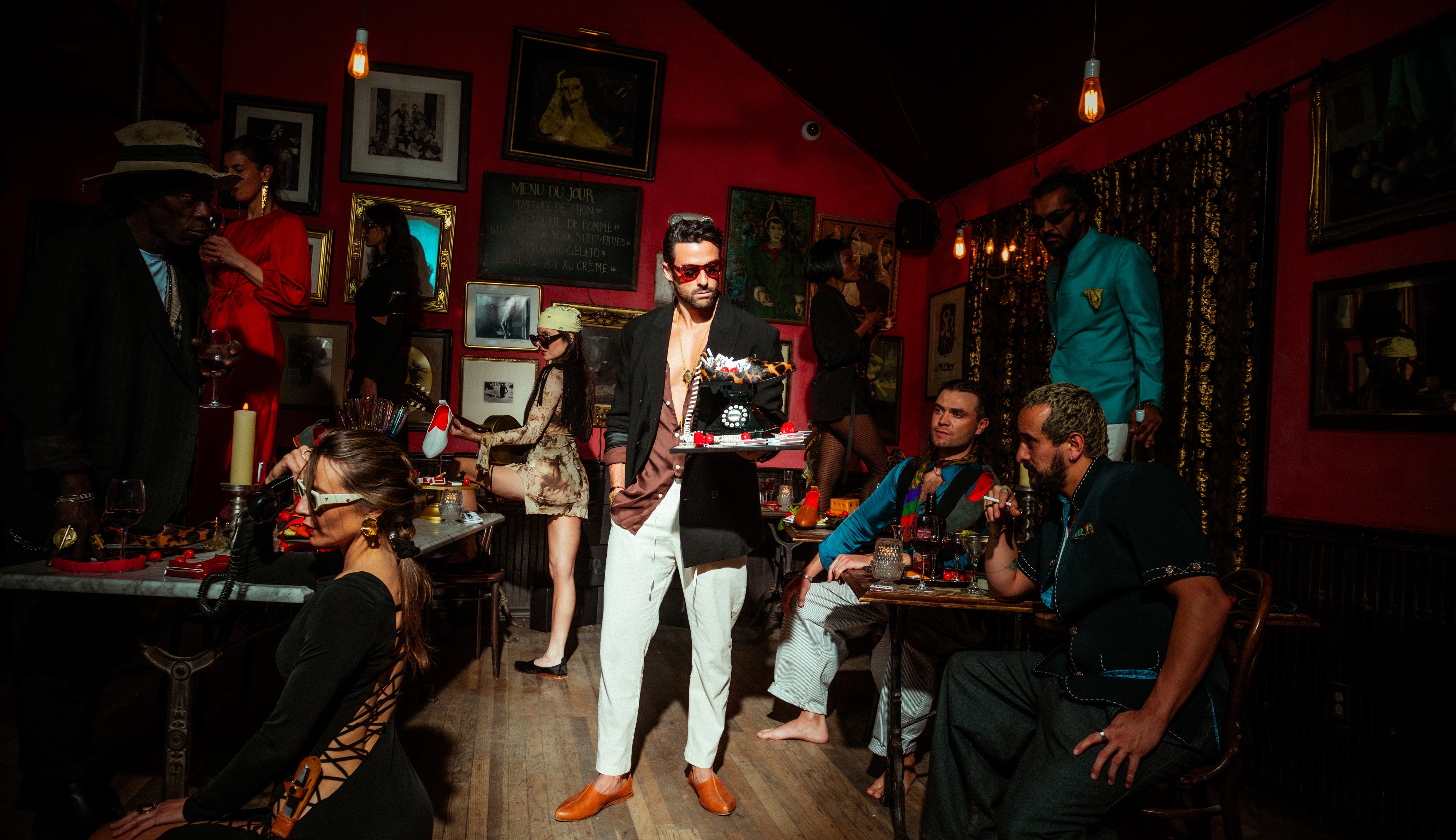 People in a dimly lit bar with red walls and framed pictures on the wall.
