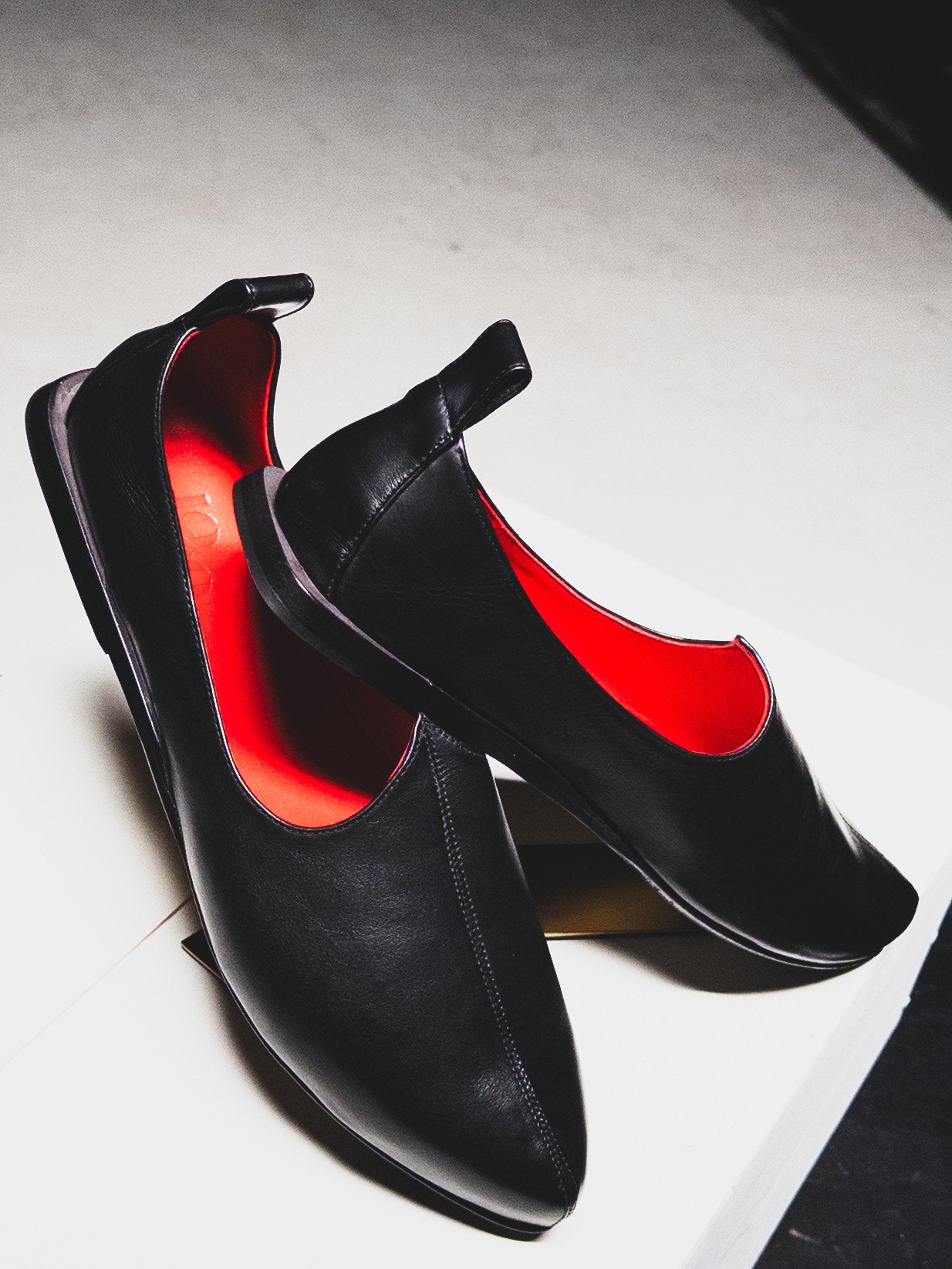 Black high-heeled shoes with red interior on a light gray background