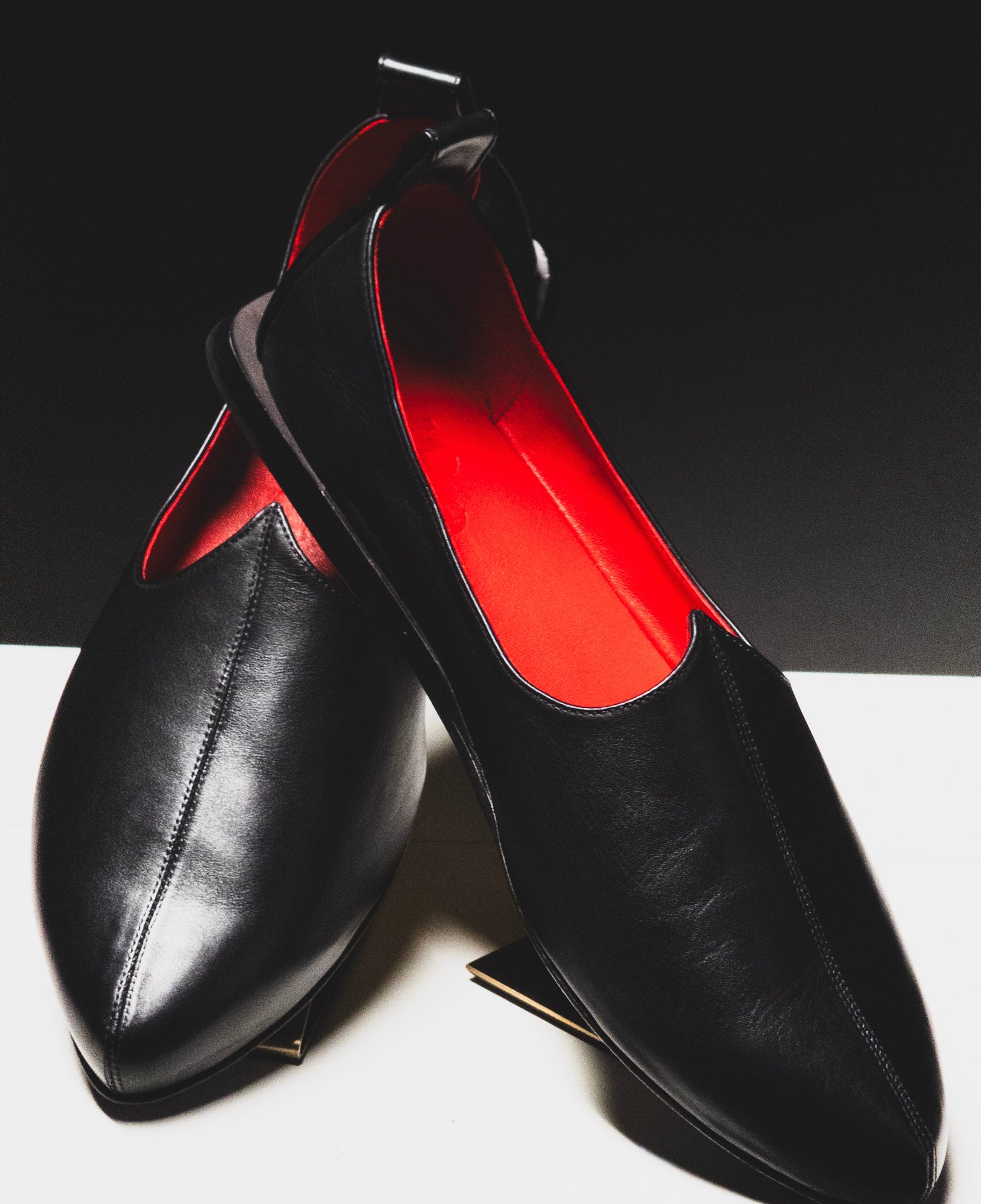 Black loafers with a red interior on a white surface and black background