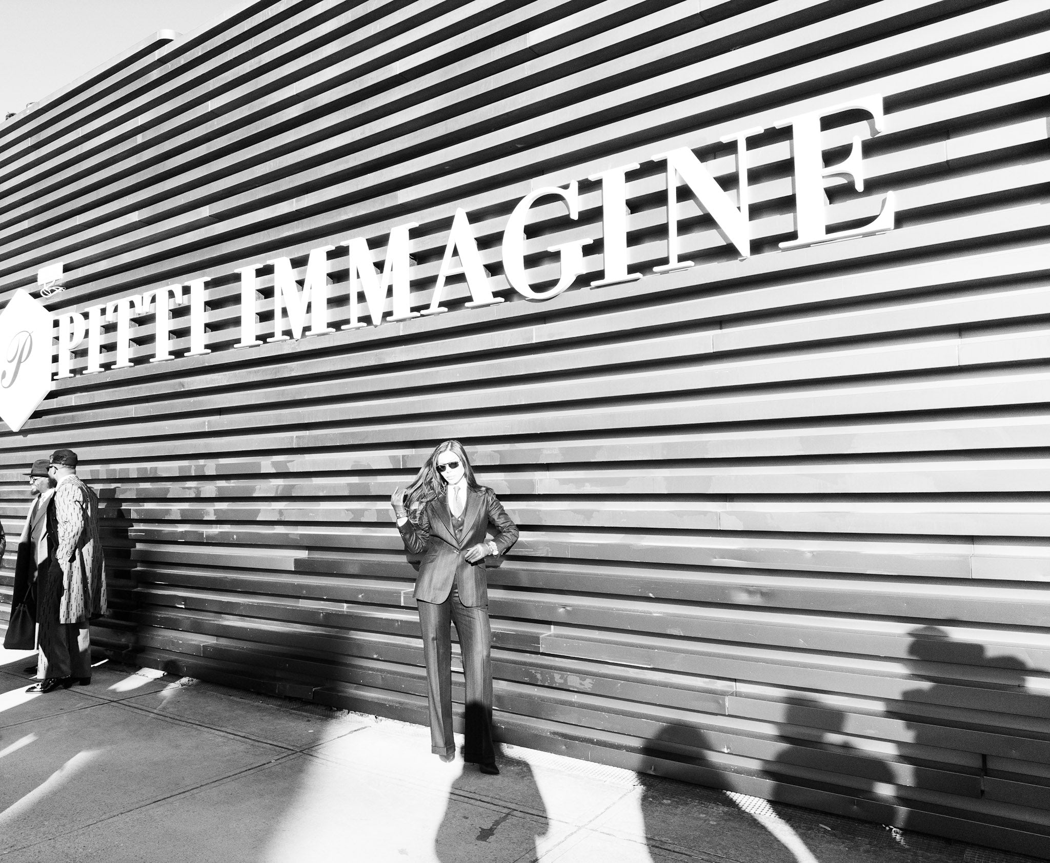 Person leaning against a building with 'PITTI IMMAGINE' sign